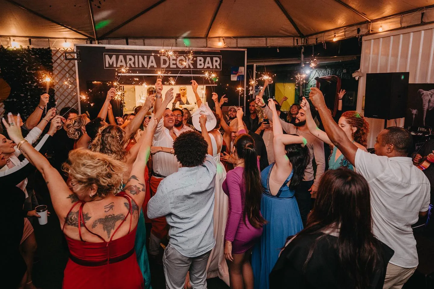 Público celebrando sob cobertura, inscrição MARINA DECK BAR ao fundo